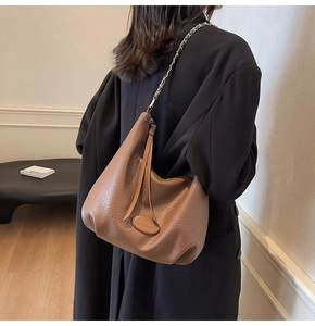 Detail of a dark brown hobo bag with litchi grain texture and metal chain strap