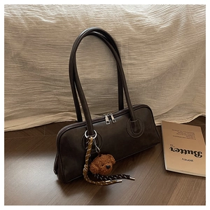 Detail of a dark brown faux leather baguette bag with a cute bear charm and silver zipper