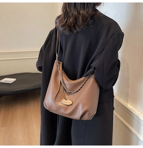 Detail of brown lychee grain leather crossbody bag with chain and oval metal plaque