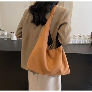 Detail of a large caramel suede tote bag worn by a model in a cozy cafe setting