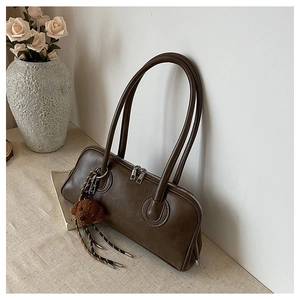 Detail of dark coffee baguette shoulder bag featuring a cute plush bear pendant accessory