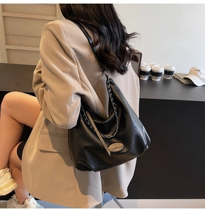 Detail view of black pebble leather tote bag with silver chain on beige blazer