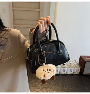 Detail einer Vintage Boston Bag in Schwarz mit weißen Nähten und Plüsch-Anhänger