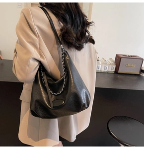 Detail of black pebbled leather hobo bag with stylish metal chain and logo plaque