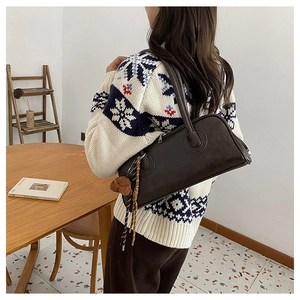 Detail of dark brown leather baguette bag with plush bear charm worn by a model