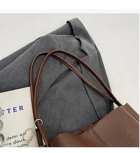 Detail of reinforced handle stitching on a brown leather tote bag with silver chain accessory