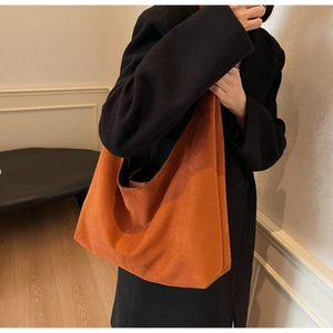 Detail of a large orange suede tote bag styled with a black coat for autumn fashion