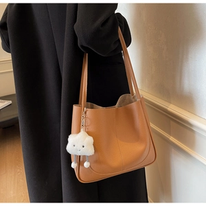 Brown litchi grain shoulder bag with white plush cloud charm on a black coat model