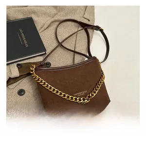 Close-up of brown suede bucket bag with gold chain strap on a blazer background
