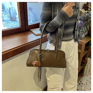 Close-up of brown Boston bag with teddy charm and decorative ribbons on a windowsill