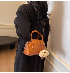 Detail der braunen Bowling-Tasche mit Bärenpfoten-Anhänger am schwarzen Wintermantel