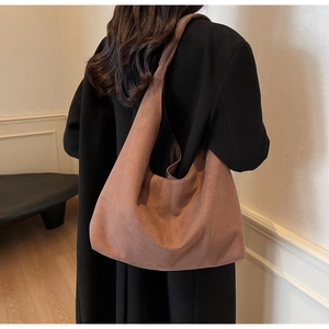 Gros plan d'un sac hobo en daim marron porté avec un manteau noir pour look d'automne