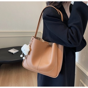 Detailed texture of brown litchi grain leather bag with a white plush cloud charm