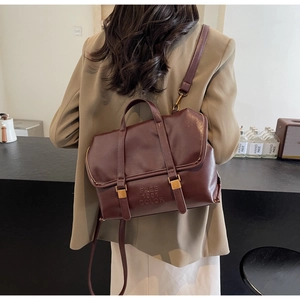 Deep burgundy leather backpack with gold buckles shown on a model in olive green suit