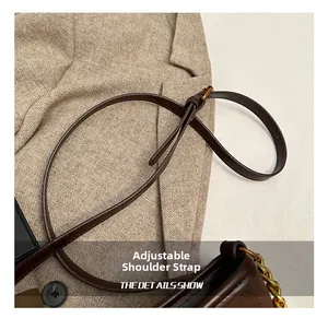 Detail of adjustable dark brown shoulder strap with gold buckle and chain on handbag