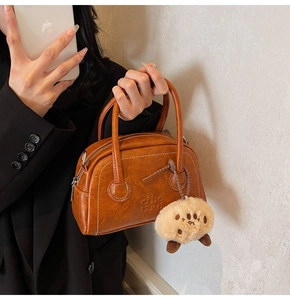 Detailansicht der braunen Bowling-Tasche mit weißen Nähten und Pfoten-Plüschanhänger