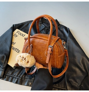 Nahaufnahme der braunen Vintage-Umhängetasche mit Plüschanhänger auf einer Lederjacke