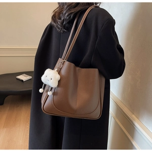 Detailed side view of a brown pebbled leather tote bag with a plush cloud charm accessory