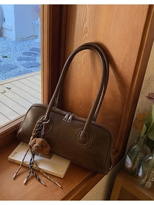Brown rectangular baguette bag with plush bear charm and dual handles on wooden windowsill