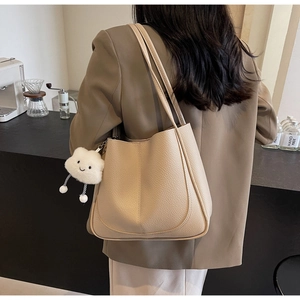 Detail of beige lychee grain tote bag with plush cloud charm in cafe setting