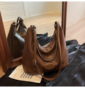 Detail of brown lychee grain leather hobo bag with stylish silver metal chain on black silk