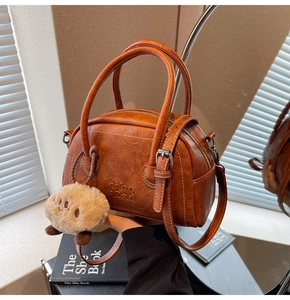 Detail einer braunen Vintage-Bowlingtasche aus Leder mit weißen Nähten und Plüschanhänger