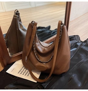 Detail view of brown pebbled leather hobo bag with silver chain on black silk