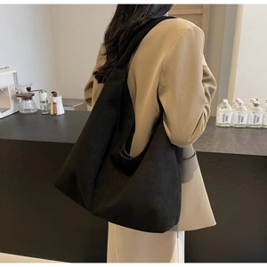 Black matte leather tote bag with wide shoulder strap worn by model in a café