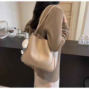 Detailed view of beige faux leather tote bag with plush ball charm and pebbled texture