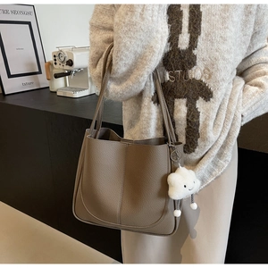Detail of brown textured leather tote bag with a white plush cloud charm on shoulder