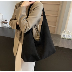 Close-up of a matte black suede tote bag with a wide strap on model in a cafe setting