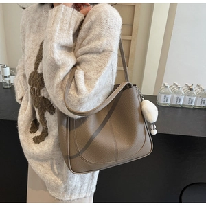Close-up of khaki pebbled leather shoulder bag featuring plush charm and elegant stitching