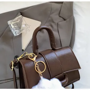 Detail view of a vintage dark brown shoulder bag with gold chain and white plush ball charm