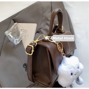 Detail of premium brown leather handbag with gold hardware hook and plush cloud charm
