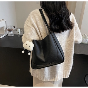 Detail view of black lychee grain tote bag with a white plush cloud charm accessory