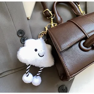 Close-up of a white plush cloud charm with a smiley face and gold metal chain hook