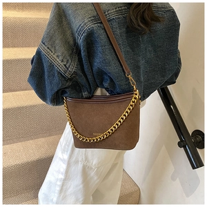 Close-up of brown suede bucket bag with gold chain and leather strap on model