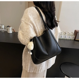Detail of black lychee texture leather shoulder bag with white fluffy charm and roomy design