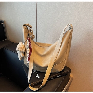 Detailansicht der großen beigen Hobo-Tasche mit Bärenanhänger auf schwarzen Büchern