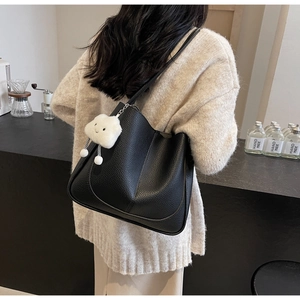 Detail of black pebbled leather tote bag with white cloud plush charm in cafe setting