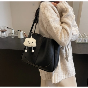 Detail of black pebbled leather tote bag with a white fluffy cloud charm on a model