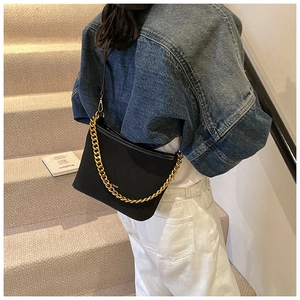 Detail of black bucket bag with chunky gold chain handle worn by model on stairs