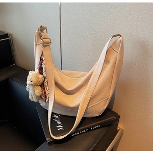Detail der beigen Halbmond-Schultertasche mit breitem Gurt und Bären-Anhänger