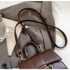 Close-up of vintage brown leather bag with golden hardware on grey suit fabric