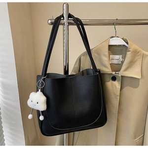 Detail of black lychee grain leather tote bag with a white cloud plush pendant charm