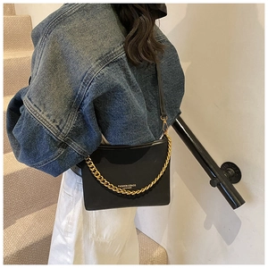 Detail of black leather bucket bag with chunky gold chain strap and metallic hardware