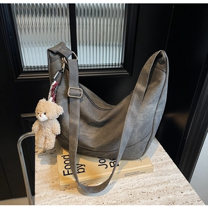 Detail der grauen Hobo-Tasche mit Plüschbären-Anhänger auf Marmoroberfläche