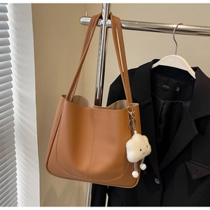 Close-up of brown textured leather tote bag with a white plush cloud charm on a metal hanger