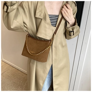 Detail of brown suede crossbody bag with gold metal chain and embossed fashion logo