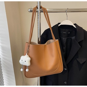 Detail of a brown lychee pattern leather tote bag with a white plush cloud accessory